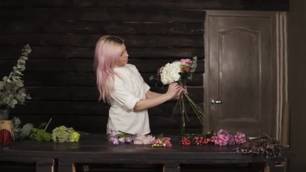 Florista menina elegante e sorridente no processo de decoração um buquê de flores. Movimento lento. Interior — Vídeo de Stock