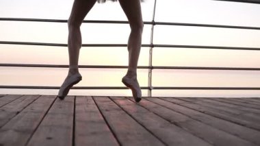 O deniz kenarında ahşap dolgu pointe egzersizleri uygulamaları iken bir bale dansçıları ayakları görüntülerini nişan al. Kadının bacakları pointe ayakkabı kapatın. Güneş doğuyor. Ağır çekim