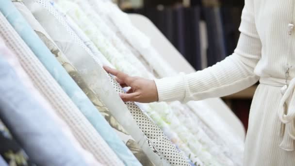 Uma linda garota compradora em uma loja de tecidos. Ela escolhe um rolo de tecido com bolinhas entre a gama de tecidos leves. Movimento lento — Vídeo de Stock