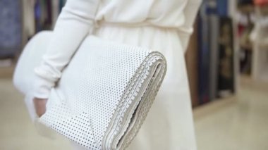 Kumaş rulo ile tekstil mağaza üzerinden yürüyen şık genç kadın Beyaz giysili. Beyaz puantiyeli ile basılmış. Ağır çekim