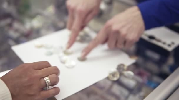 Deux femmes comptent et sélectionnent les boutons en tissu sur une table en verre dans un magasin de tissus. Client et vendeur. Les mains seulement. Extrêmement près — Video