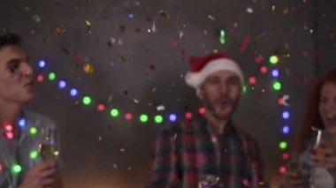 Group of friends celebrating enjoying new years eve party having fun celebration. Friendly and joy. Happy emotion. Christmas decorations at home. Man exploding confetti stick, clinking glasses with