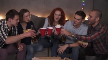 Çeşitli arkadaş gruplarının portresi kutlama için pizza dağıttı. Mutlu bir şekilde bira içiyorlar, şerefe. Yakın arkadaşlarından oluşan bir şirkette çelenk ışıklarıyla süslenmiş rahat bir odada eğlenceli bir parti.