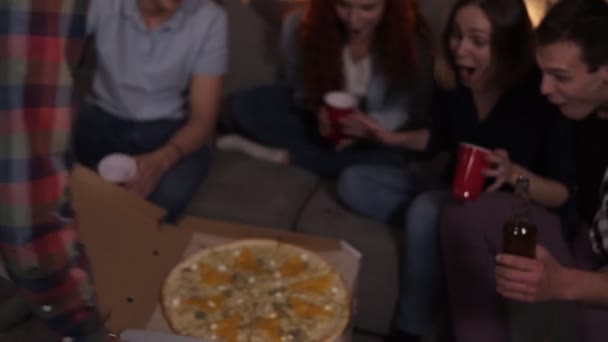 Happy friends got delivery pizza and celebrating party clinking bottles and red cups with beer and soda sitting on sofa at home. So excited about big pizza party — ストック動画