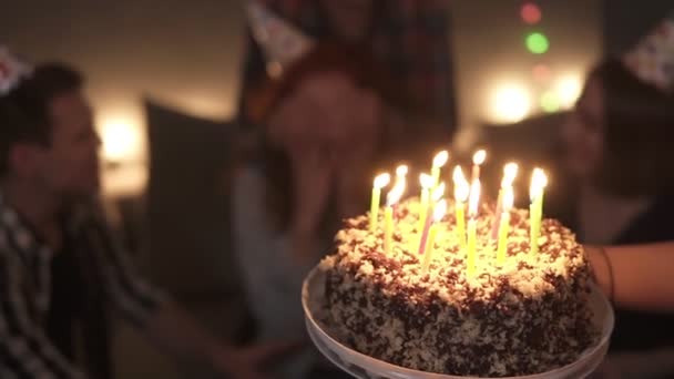 Närbild, fokus på födelsedagstårta med brinnande ljus. Glad leende lockigt rödhårig flicka förväntar sig överraskning med slutna ögon av sin vän bakom. Blåser ljus ut på hennes lilla — Stockvideo