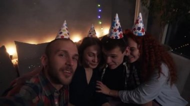 Genç mutlu arkadaşlar ya da iki çift, küçük, samimi bir doğum günü kutlaması yapıyorlar. Kutlama konileri içinde oturup selfie çekiyorlar ya da kameraya bakıyorlar. Doğum gününü kutluyor, onu öpüyor.