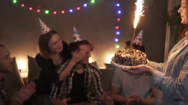 Freunde feiern Geburtstagsparty, überraschen Freund mit Kuchen mit brennendem Sekt. Superaufgeregter Mann, der lacht und seine Freunde umarmt. zusammenkommen. engsten Freunden. Lichtergirlanden auf dem — Stockvideo