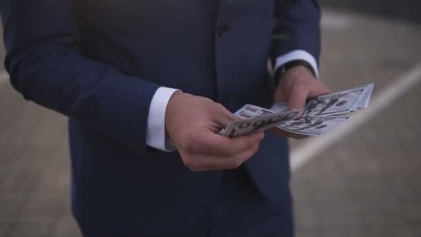 Un hombre de negocios rico y sólido en la calle sosteniendo un paquete de dinero americano en sus manos, contándolo. Un hombre rico cuenta cientos de billetes, con traje azul. Sin cara. — Vídeo de stock