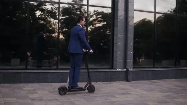 Ofisteki bir iş görüşmesi için elektrikli scooter kullanan genç bir işadamı, ofis binaları, iş adamı, elektrikli taşımacılık, ekolojik ulaşım. Yan görünüm — Stok video