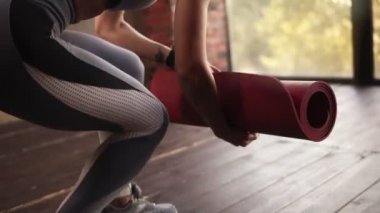 Panoramik pencereli boş stüdyoda ders hazırlama süreci. Genç kadın fitness stüdyosunda kırmızı yoga minderini parçalıyor. Özgürlük, sağlık yaşam tarzı konsepti. Yakın çekim. Yavaş çekim