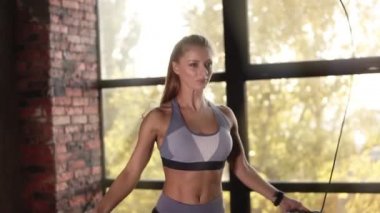 Spor salonunda ip atlarken at kuyruklu bir fitness kadınının kesilip kapatıldığı görüntüler. Boş stüdyoda ip atlama egzersizi yapan güzel kız. Ciddi bir kadın kardiyo yapıyor.