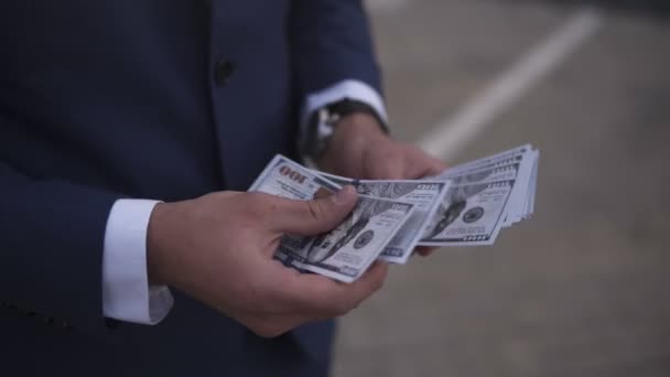 Unrecognizable businessman on the street holding bundle of american money in his hands, counting it. Wealthy male counts hundred banknotes, wearing blue suit. Close up — Stock Video