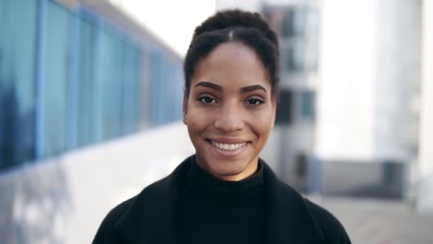 Portrét krásné stylové africké Američanky usmívající se na kameru, která vypadá sebevědomě. Na sobě černé šaty, městské zázemí. Řada Real People — Stock video