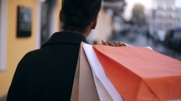 Omzunda renkli alışveriş torbalarıyla caddede yürüyen Afro-Amerikan bir kızın nadir görüntüsü. Tasasız genç bir kadın lüks caddelerde alışveriş yaptıktan sonra yürüyor, geçmişi bulanık — Stok video