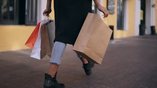  ztratí ženy nohy nosí stylový černý kabát a džíny v den, kdy držet barevné nákupní tašky po velkém nákupním dni. Módní nakupující nakupující ve zpomaleném filmu. Vzácné zobrazení