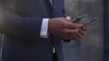 Sokakta tanınmayan bir iş adamı elinde bir tomar Amerikan parasını tutuyor, sayıyor. Zengin erkek, mavi takım elbiseli, 100 banknot sayıyor. Kapatın. Yan görünüm, bulanık arkaplan