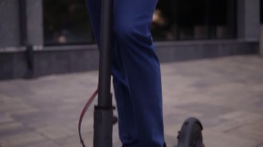 Zarif mavi takım elbiseli ve dışarıda duran gözlüklü genç bir iş adamının görüntüsü. İş binasının önünde elektrikli scooterıyla yakışıklı bir iş adamı.