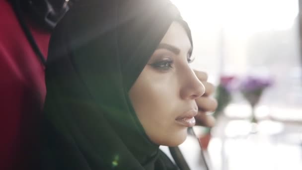 Linda menina maquiagem perfeita com hijab preto árabe tradicional. Mulher irreconhecível nas costas a pentear a cobertura. Vista lateral. Luz solar no fundo — Vídeo de Stock