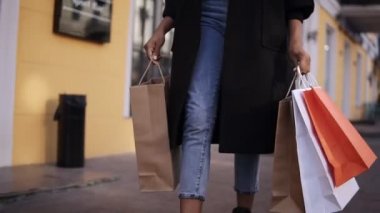  Gündüz vakti şık siyah ceket ve kot pantolon giyen kadın bacaklarından kurtul. Büyük alışveriş gününden sonra renkli alışveriş torbaları tut. Moda alışverişçisi yavaş çekimde alışverişe çıkıyor.
