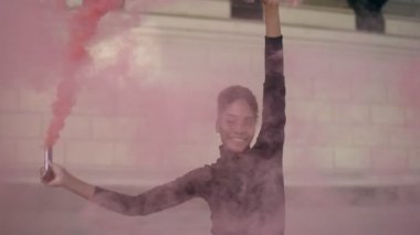 Pembe dumanlı bomba ya da parlak tuğlalı arka planda el bombası olan güzel bir Afro-Amerikalı kadın. Siyah kazaklı ve kot pantolonlu el bombası sallayan ve rahatça dans eden bir kız. Yavaş çekim
