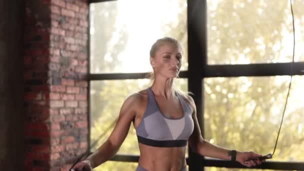 Athletic beautiful blonde woman wearing sportswear exercises with skipping rope in the empty gym or studio. Fitness training using jumping rope cardio workout. Close up — Stock Video