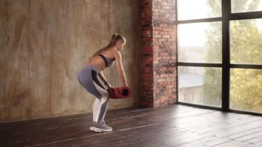 Panoramik pencereli boş stüdyoda ders hazırlama süreci. Genç kadın fitness stüdyosunda kırmızı yoga minderini parçalara ayırıyor. Oturup vücut çalışmasına hazırlanıyor. Özgürlük, sağlık yaşam tarzı konsepti