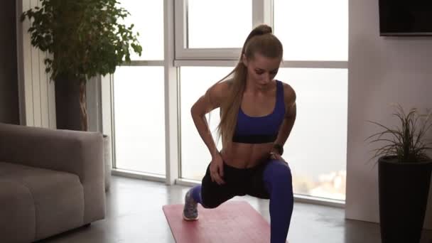 Jonge fit vrouw in sportkleding doet stretching lunge oefening binnen, thuis interieur. Activiteit en gezonde levensstijl. Vooraanzicht — Stockvideo