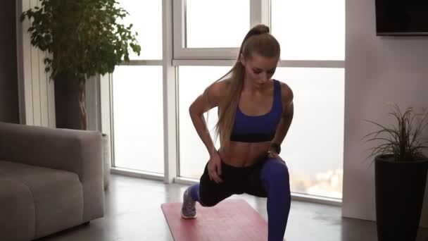 Young fit female in sportswear doing stretching lunge exercise indoor, home interior. Activity and healthy lifestyle. Front view — Stockvideo