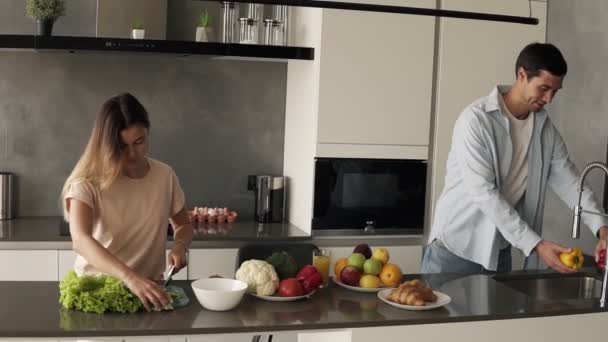 Alegre joven familia pareja cortar ensalada de verduras frescas, divertirse cocinar juntos im moderna loft interior cocina, marido feliz ayudar a preparar comida saludable lavado de peper amarillo en el fregadero — Vídeos de Stock