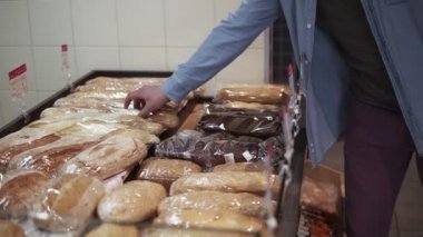 Kafkasyalı stil sahibi bir adamın, süpermarketteki en iyi ekmeği fırın tezgahından seçmesi. Akşam yemeği için küçük bir Fransız ekmeği seç. Yan görünüm