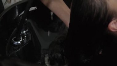 Tanınmaz hale gelen kuaför esmer kadın saçlarını yıkıyor. Makyaj ve güzellik salonu. Siyah lavaboda, saçı ıslak bir kuaförün elini kapat.