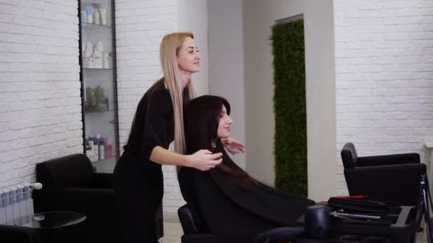 Joven, hermosa mujer mirando al espejo después de corte de pelo terminado. Peluquería clientes ondeando pelo castaño largo después de corte de pelo. Filmación de una hermosa chica morena en la barbería. Vista lateral — Vídeos de Stock