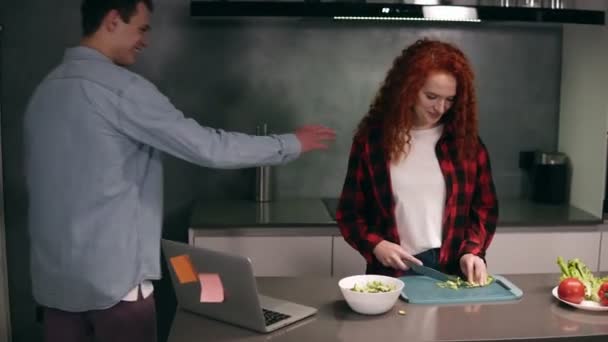 Casal engraçado enquanto cozinhando juntos na cozinha de cor cinza, jovem família ativa se divertindo rindo se sente cuidado.Homem feliz veio à cozinha depois do trabalho para obter ajuda, desfrutar de alimentos de preparação — Vídeo de Stock