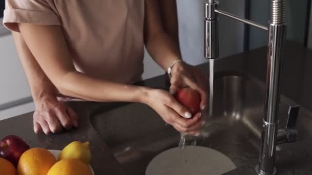 La coppia amorevole irriconoscibile lava la frutta fresca in lavandino prima di mangiare di mattina sulla cucina moderna. Uomo in jeans accarezzando delicatamente la schiena della sua premurosa moglie — Video Stock