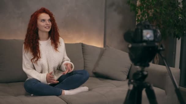 Curly red headed young girl vlogger is talking in front of camera recording video for online blog in internet speaking, smiling and gesturing. Woman is wearing jeans and white sweater. Accelerated — Stock Video