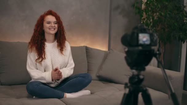 Caucásico cabeza roja joven vlogger está hablando delante de la cámara de vídeo de grabación para el blog en línea para sus seguidores, sonriendo y haciendo gestos. La mujer lleva vaqueros y suéter blanco. Acelerado — Vídeo de stock