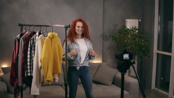 Attrayant styliste enregistrement vidéo pour blog en ligne montrant des vêtements à la mode de sa garde-robe, parler et gestuelle en utilisant la caméra dans le salon. Blogging, personnes heureuses et concept internet — Video