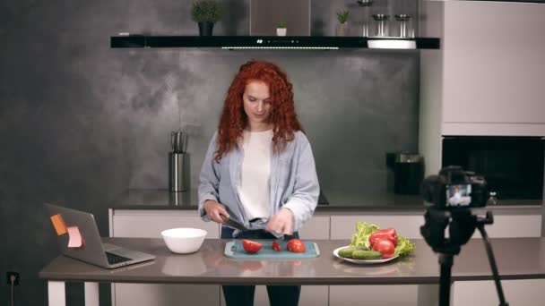 カジュアルな服の若い女性は料理ブログをリードし、灰色のキッチンでビデオを記録します。ブログのビデオ撮影-ダッシュボード上の赤いヘッドカットトマト。現代のマーケティング、ソーシャルネットワーク — ストック動画