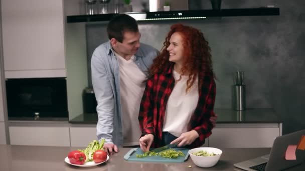 Casal engraçado enquanto cozinhando juntos na cozinha de cor cinza, jovem família ativa se divertindo rindo se sente cuidado.Homem feliz veio à cozinha depois do trabalho para obter ajuda, desfrutar de alimentos de preparação. Abraço — Vídeo de Stock