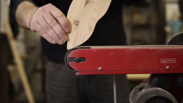 El hombre muele el patrón de forma de pez con la máquina de pulir con aserrín volando hacia los lados, profesión, concepto de carpintería. Primer plano del hombre lijando madera en el taller. Movimiento lento — Vídeo de stock