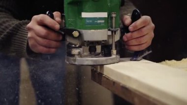 Ahşap atölyesinde elle öğütme makinesiyle çalışan bir zanaatkârın elleri son derece yakındır. Büyük ahşap bir tahta öğütüyor. Toz ve cips yerlere saçılıyor. Tanımlanamaz