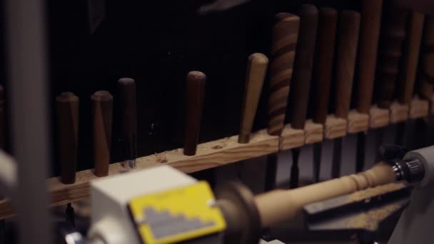 Uit de verscheidenheid van gereedschappen kiest de mens de juiste grootte schaafmachine. Timmerman mannelijke handen snijden houten knop uit hout stuk spinnen op de machine met behulp van beitel, werken aan de vorm, decoratie. Langzame beweging — Stockvideo