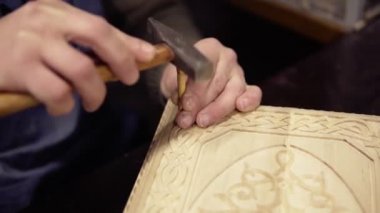 Tavlada ahşap süslemeler yapan bir zanaatkar çalışma yerinde oturuyor. Küçük tahta sopa ve çekiçle detaylar üzerinde çalışan bir adamın görüntülerini kapat.