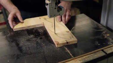 Elektrikli kesme makinesiyle çalışan erkeklerin görüntülerini kapatın. Masadaki balık şeklindeki ahşap deseni kesen bir adamın yüksek açılı görüntüleri.