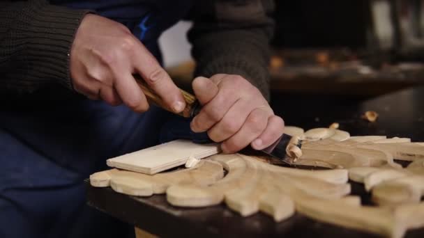 Повільний рух тесля, який працює на дерев'яній майстерні на столі, готує деталь дерев'яного виробу, частину майбутніх меблів. Крупним планом кадри рук чоловіка вирізають візерунки з — стокове відео