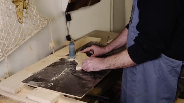 El hombre muele el patrón de forma de cola de pescado con la máquina de pulir con aserrín volando hacia los lados, profesión, concepto de carpintería. Vista lateral de un hombre lijando madera en el taller. Movimiento lento — Vídeo de stock