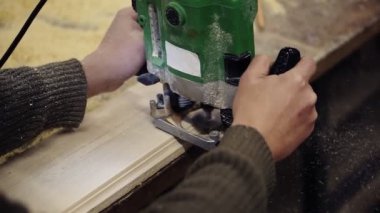 Ahşap atölyesinde elle öğütme makinesiyle çalışan bir zanaatkârın ellerinin görüntüsü. Büyük ahşap bir tahta öğütüyor. Toz ve cips yerlere saçılıyor.