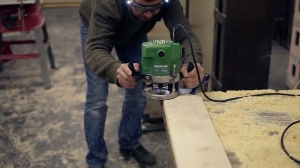 Trabajador carpintero masculino en gafas protectoras muele la barra de madera. Pulido artesanal con rectificadora manual en taller de madera. Vista frontal — Vídeos de Stock
