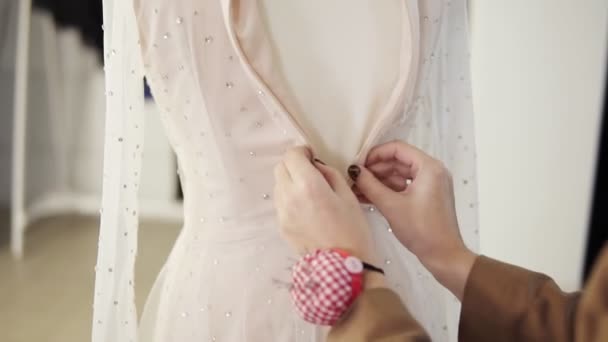 Nerozpoznatelný ženský krejčí upevnit základ oděvu na šumivé svatební šaty na figuríny v jasném studiu. Detailní záběr ženských rukou zapínání šaty na zádech — Stock video