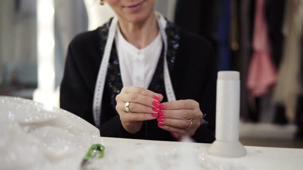 Zeitlupe einer Schneiderin mit Maßband am Hals, die den Nadelfaden einlegt, um den Stoff von Hand zu nähen, um ein Kleidungsstück zu schaffen. Frontansicht — Stockvideo